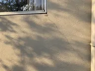Hairline crack running diagonally from a window corner across cream render